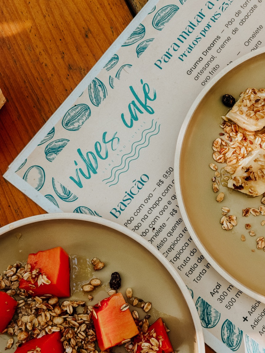 Cardápio impresso do Vibes Café sobre a mesa, com pratos de mamão e granola